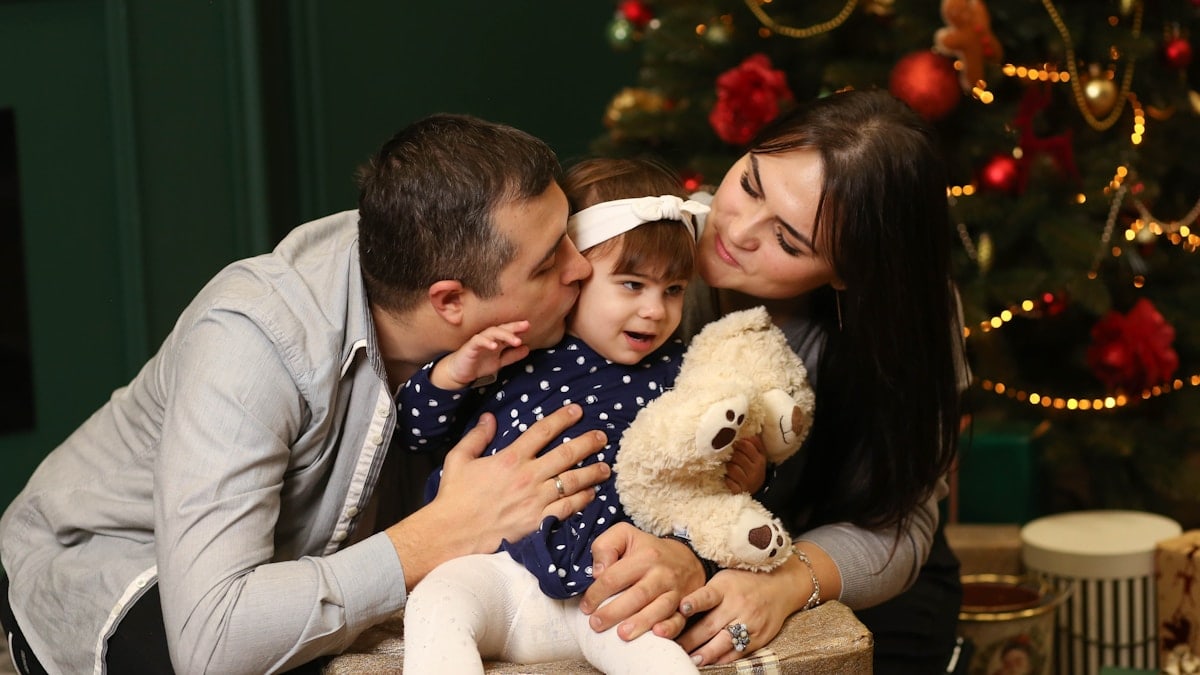 a man and a woman holding a baby and a teddy bear